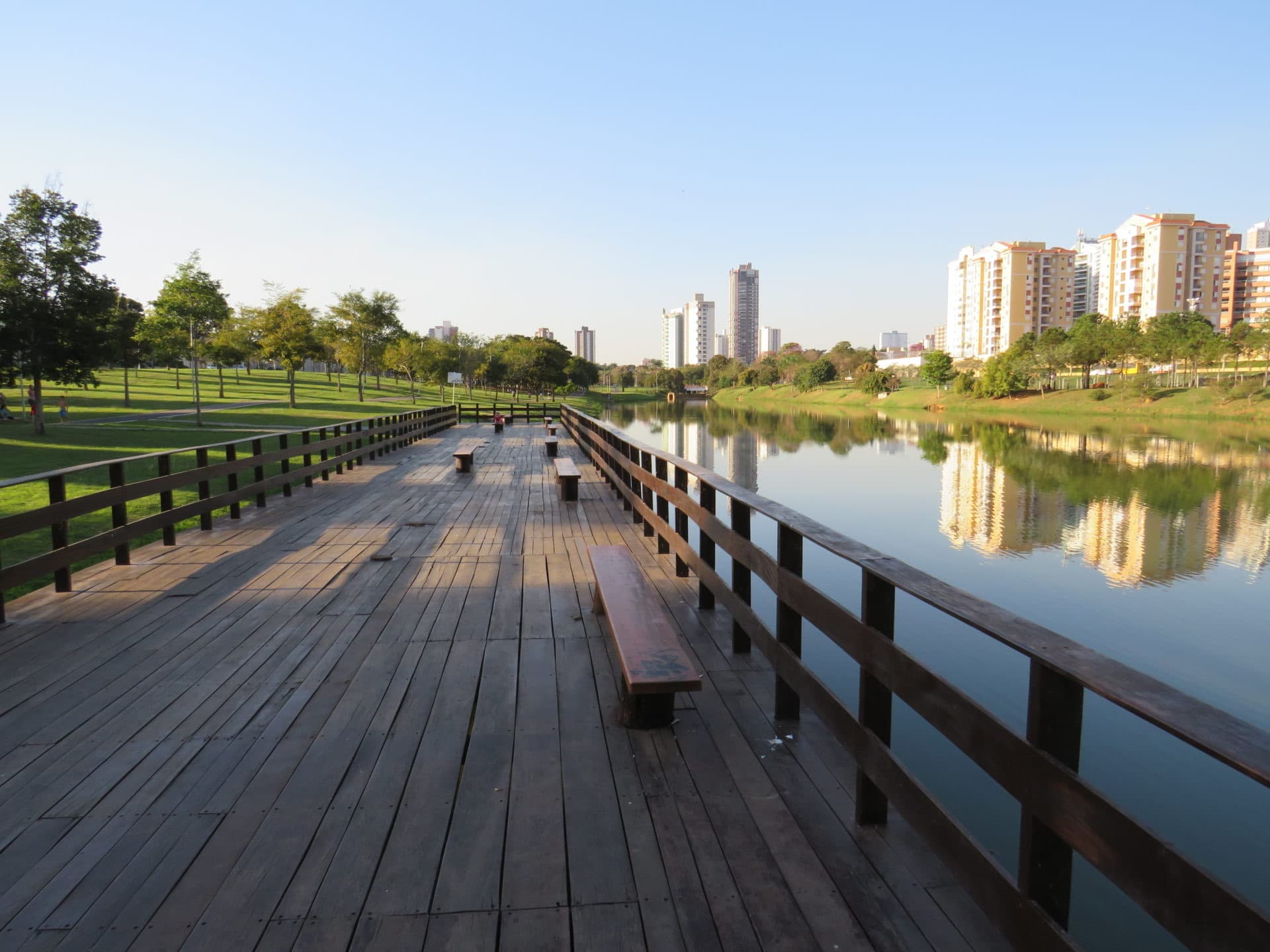 Deck de madeira sobre o lago do Parque Ecológico, com a cidade ao fundo